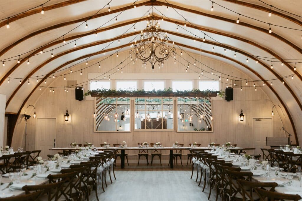 Rustic wedding barn venue with chandeliers, string lights, and elegantly set tables for a charming reception.