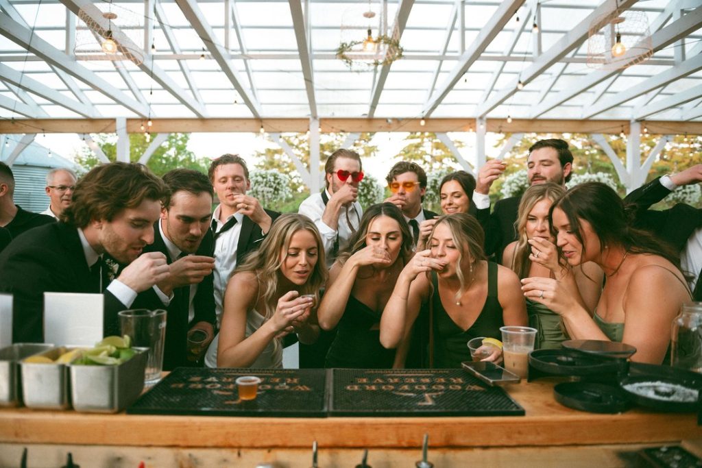 Group of friends enjoying celebratory drinks at a lively party under a decorated outdoor pavilion.