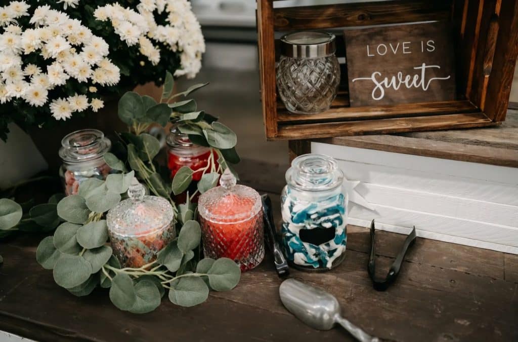 Assorted candies in glass jars with flowers and Love is sweet sign at rustic wedding candy table.