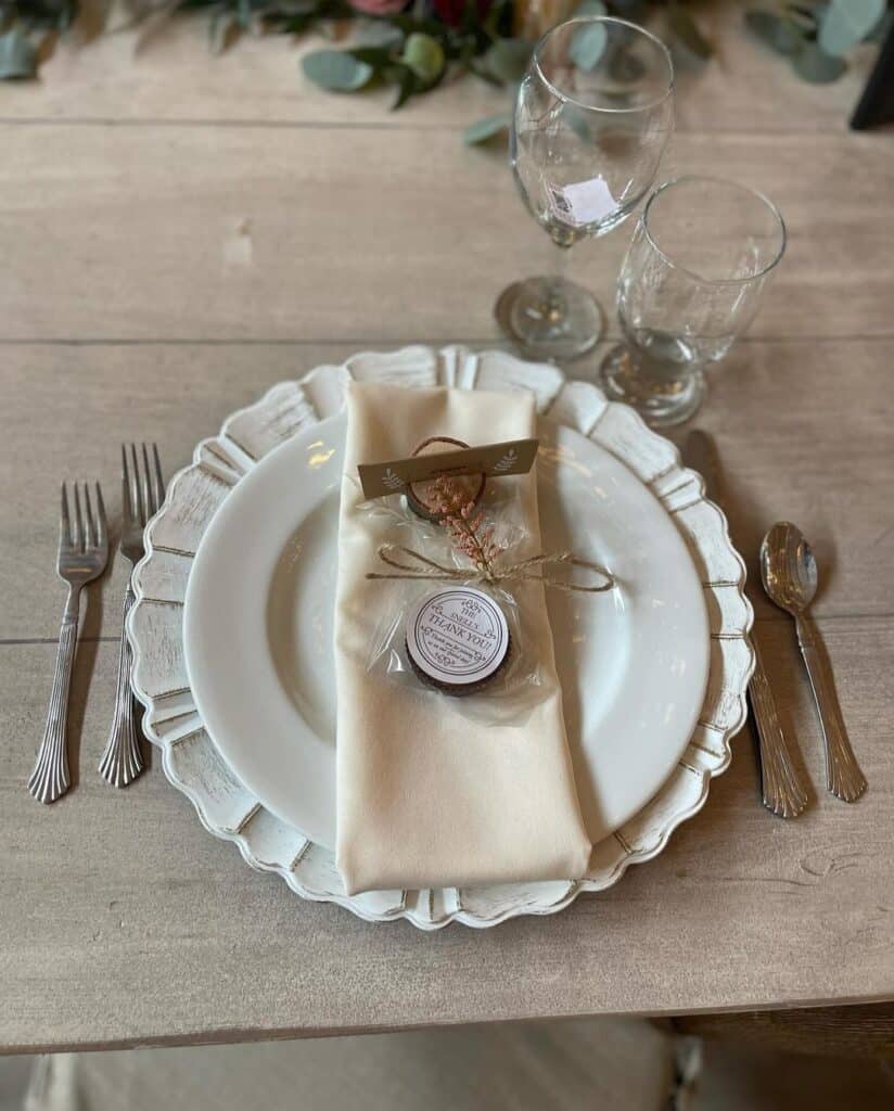 Elegant table setting with white plate, cream napkin, and glassware on rustic wooden table. Perfect for weddings or events.